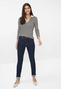 Haut à rayures à manches longues avec un col beige, associé à un jean en denim foncé avec des ourlets retroussés et des détails de couture subtils.