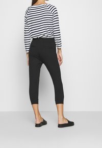 Des pantalons noirs, coupés, avec une taille élastique et des poches au dos, associés à un haut à manches longues rayé avec une coupe décontractée.