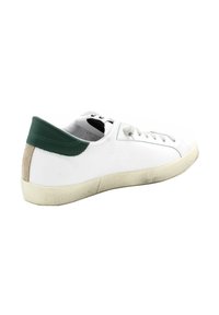 Sneaker bianca in pelle con un tallone in suede verde e beige, punta rotonda, lacci grigi e una suola in gomma testurizzata con segni di usura visibili.