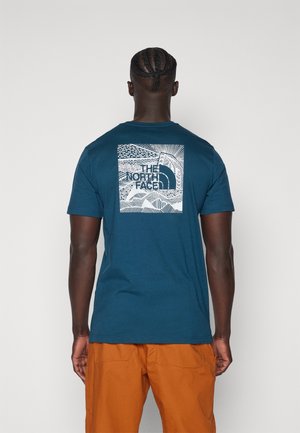 Teal katoen t-shirt met een witte grafische print op de achterkant met abstracte patronen en de tekst "THE NORTH FACE" in het midden.