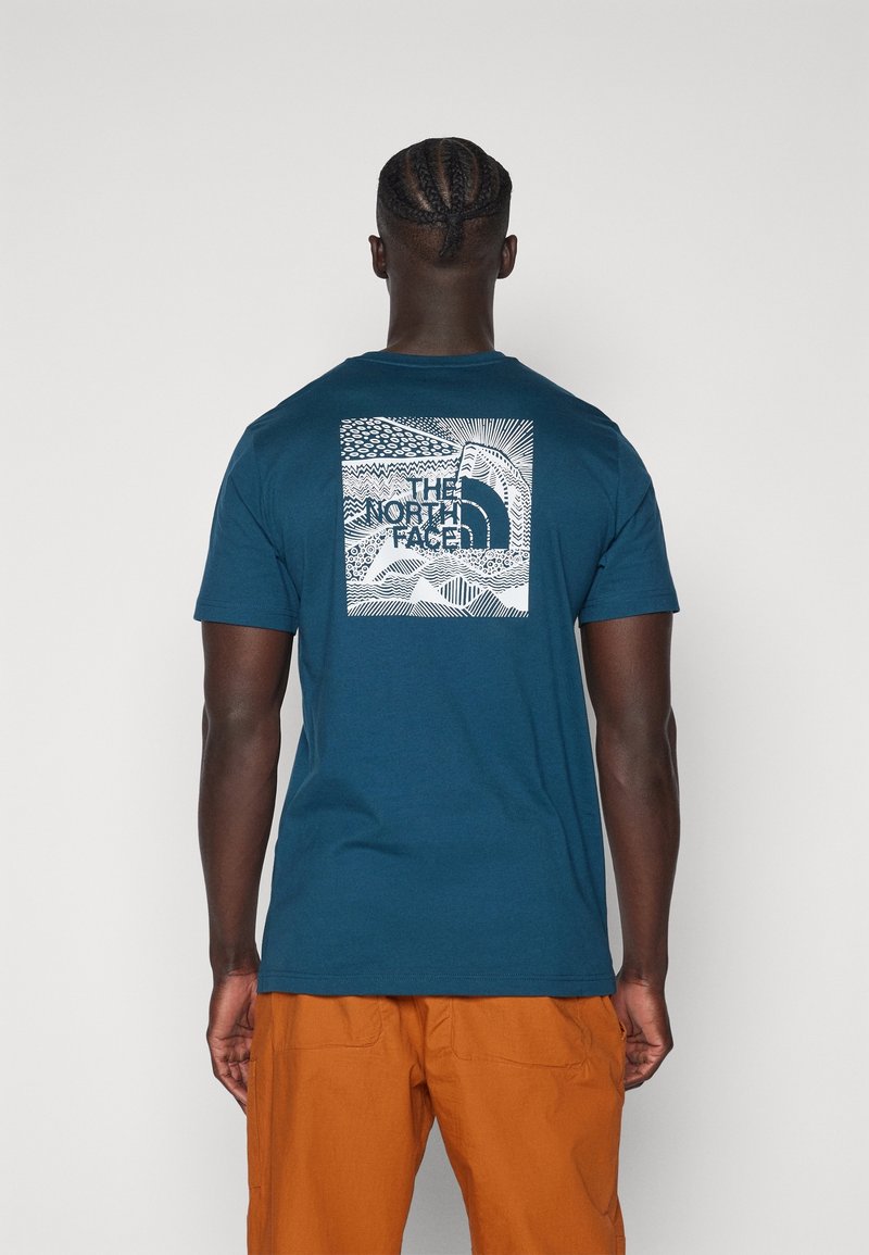 Teal Baumwoll-T-Shirt mit einem weißen Grafikdruck auf der Rückseite, der abstrakte Muster und den Text "THE NORTH FACE" in der Mitte zeigt.