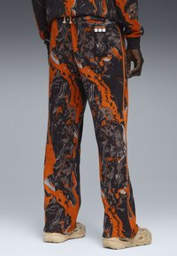 Sweatpants i sort og orange med mønstrede marmorlignende svirls, elastisk talje og afslappet pasform. Har sideløbere og markante design detaljer.