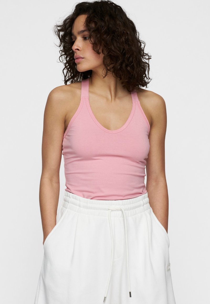 Top de tirantes sin mangas de color rosa, hecho de una tela suave, con un escote redondo y tirantes finos, combinado con pantalones blancos con cordón.