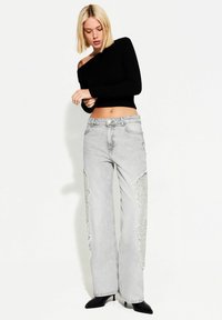 Lys grå vidde jeans med slidte patchwork og knaplukning, parret med en tætsiddende sort langærmet top. Glat tekstur.