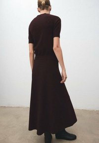 Vestido de punto marrón ajustado con mangas cortas y falda acampanada. El diseño presenta una textura suave y una costura sutil en la cintura.