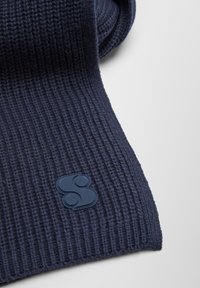 Écharpe en maille côtelée bleu marine avec une finition texturée et un grand patch logo bleu à une extrémité.