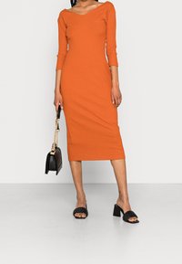 Robe midi orange côtelée avec un col en V et des manches trois-quarts, accompagnée de sandales à glisser tissées noires et d'un sac à main noir avec une chaîne dorée.