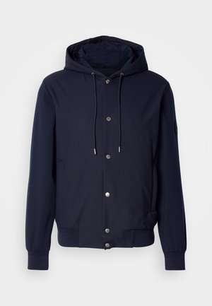 Sötétkék kapucnis dzseki elől patent gombokkal, húzózsinóros kapucnival, bordás mandzsettákkal és oldalsó zsebekkel.