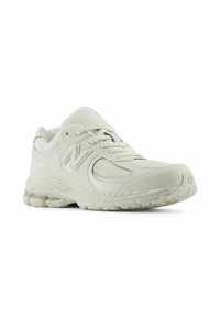 Baskets blanches avec une tige en cuir lisse et en mesh, semelle texturée, fermeture à lacets et un grand logo "N" sur le côté.