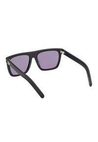 Occhiali da sole neri con finitura opaca, lenti viola, forma quadrata e aste sottili; presenta un logo verde sulla tempia sinistra.
