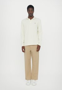Cămașă polo cu mânecă lungă, de culoare bej deschis, dotată cu guler, asortată cu pantaloni largi bej și adidași albi. Design simplu, cu accesorii minimale.