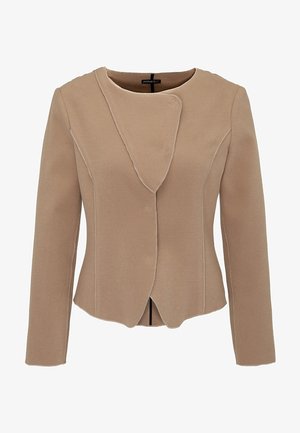 Beige räätälöity takki, jossa on uniikki epäsymmetrinen kaulus, pitkät hihat ja ommellut yksityiskohdat. Pehmeä, teksturoitu kangas.