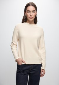 Maglione a coste di un beige chiaro con maniche lunghe, scollatura a girocollo e una vestibilità comoda, abbinato a jeans in denim blu scuro.