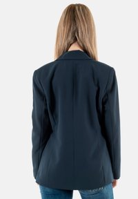 Blazer azul marino con un corte ajustado, solapas muestradas y una textura suave. Presenta hombros estructurados y una parte trasera entallada.