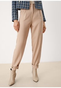 Beiga högmidjade byxor med veck och uppvikta fållar, tillsammans med beiga spetsiga ankelstövlar. Mjuk tyg och lös passform.