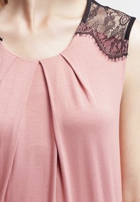 Bluzka w odcieniu różowego różu z fałdami przy dekolcie i czarnymi koronkowymi akcentami na ramionach, co tworzy teksturalny kontrast.