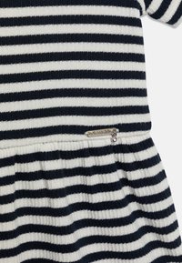 Sukienka w paski w kolorze granatowym i białym, o prążkowanej fakturze, z opuszczoną talią i metalowym logo z małym detalem z cyrkonii.