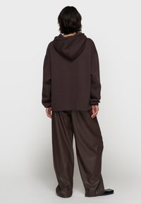 Brązowy, oversize'owy hoodie z kapturem na sznurek, w połączeniu z luźnymi, ciemnymi, ekologicznie skórzanymi spodniami. Gładka faktura, swobodny krój.