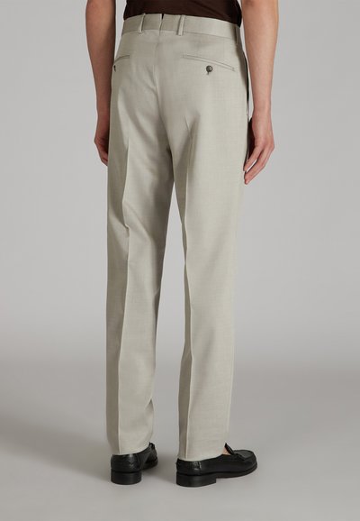 Jasno beżowe spodnie z teksturowanej tkaniny, prosty krój nogawki, dwie tylne kieszenie z guzikami, noszone z czarnymi półbutami.