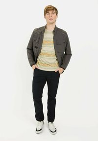 Grijze gewatteerde jas, gestreepte gele en groene t-shirt, zwarte broek en witte sneakers. Bevat borstzakken en heeft een slank ontwerp.