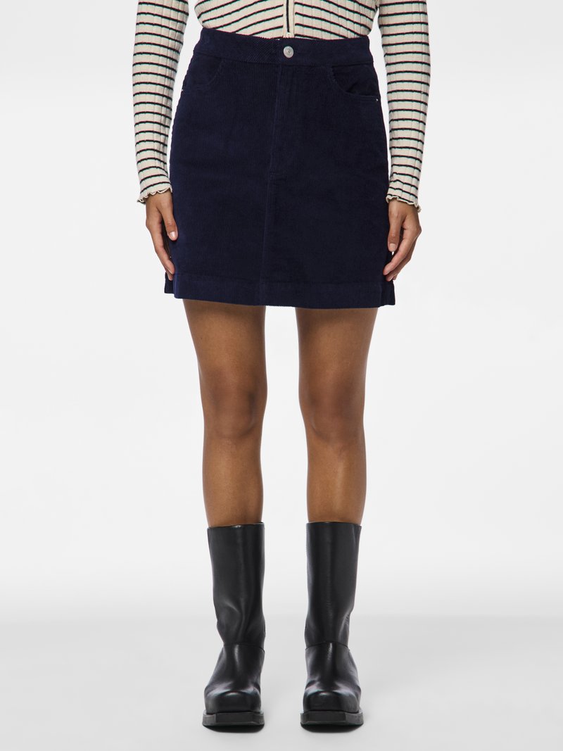 Μίνι φούστα από σκουρόχρωμο καρό με μπροστινή κουμπί, δύο πλαϊνές τσέπες και ίσια εφαρμογή, συνδυασμένη με μαύρες μπότες μέχρι το γόνατο.