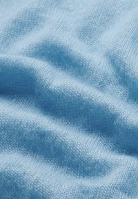 Hellblauer Strickstoff mit einer weichen, strukturierten Oberfläche, der feine Wellenmuster und unterschiedliche Garnstärken aufweist.