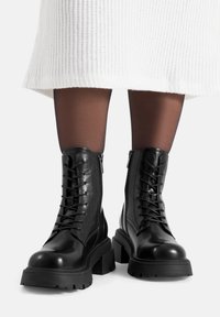 Czarne skórzane botki za kostkę z przodem na sznurowadła, bocznymi zamkami i grubymi gumowymi podeszwami, o gładkiej teksturze i zaokrąglonym kształcie noska.
