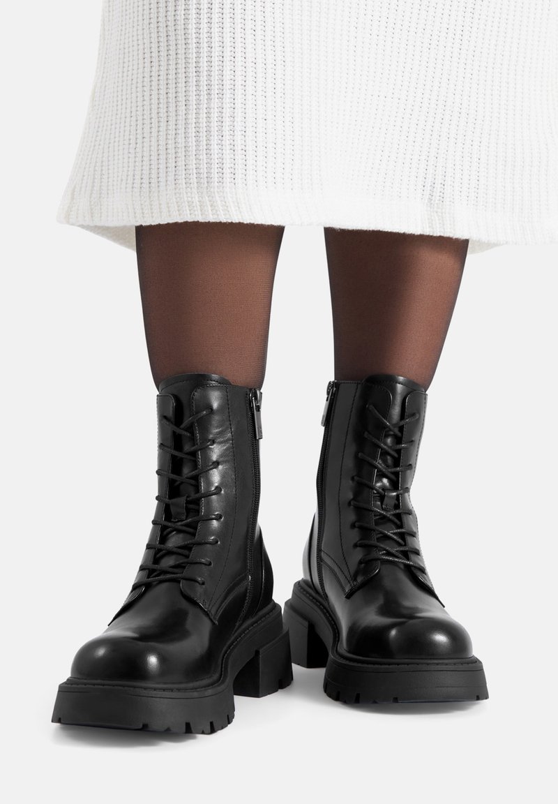 Czarne skórzane botki za kostkę z przodem na sznurowadła, bocznymi zamkami i grubymi gumowymi podeszwami, o gładkiej teksturze i zaokrąglonym kształcie noska.