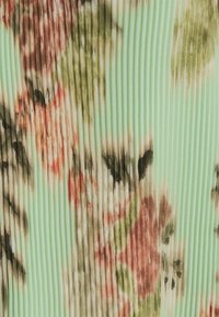 Blumenmusterstoff in Grüntönen, Pfirsichtönen und Braun, mit vertikalen Falten, die Textur und Tiefe erzeugen.