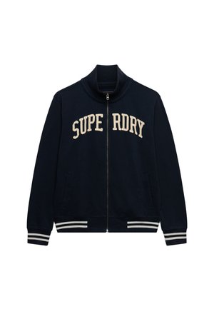 Veste bleu marine zippée avec col montant, texte beige "SUPERDRY" sur la poitrine, poignets et ourlet à rayures blanches. Deux poches avant.