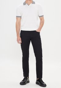 Bílá polokošile s límečkem a černým proužkovaným lemováním. Kombinována s černými úzkými kalhotami a černými teniskami.