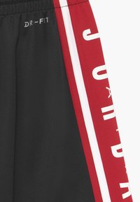 Black athletic shorts made of moisture-wicking fabric. Features a red side panel with white stripes and bold white "JORDAN" text.