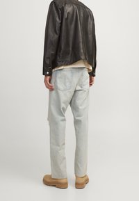 Svart läderjacka med en avslappnad passform, ljusblå slitna jeans och bruna boots. Jackan har en något kortad design och knappar som detaljer.