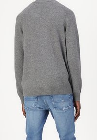 Suéter de lana gris con ribetes en los dobladillos y puños, que presenta un cuello redondo clásico y un ajuste holgado. Se lleva con jeans de mezclilla claros.