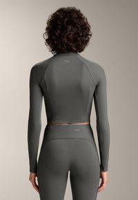 Sivý športový top s dlhými rukávmi a rebrovanou textúrou, skombinovaný s legínami vysokého pásu v rovnakom štýle. Obsahuje značkové akcenty na oboch odievoch.