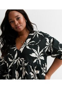 Schwarzes Kleid mit großem weißen Blumenmuster, V-Ausschnitt, kurzen Puffärmeln und gerafftem Saum. Hergestellt aus leichtem Stoff.