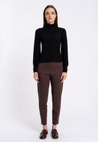 Czarny golf z długim rękawem, zestawiony z brązowymi, dopasowanymi spodniami. Buty to błyszczące, ciemnoczerwone mokasyny. Prosty i dopasowany krój.