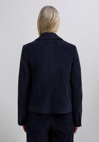 Navy corduroy blazer with a ribbed texture, notch lapel, and button accents on the sleeve. Tailored fit and single back vent.