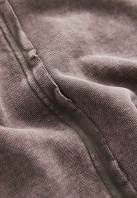 Tessuto grigio che mostra un primo piano della texture liscia con dettagli delle cuciture visibili. La superficie presenta leggere variazioni e imperfezioni.