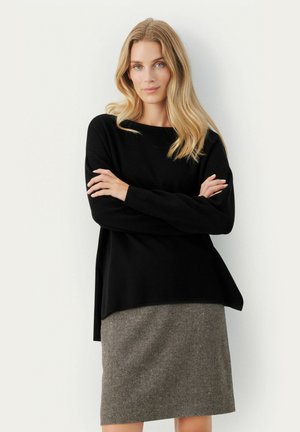 Maglione nero a maniche lunghe con vestibilità ampia e scollatura rotonda, abbinato a una gonna grigia con texture a lunghezza ginocchia caratterizzata da un motivo sottile.