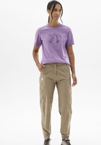 T-shirt en coton violet avec un graphisme de montagne noire, associé à un pantalon cargo marron clair avec des poches et un logo sur la jambe.