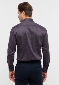 Camicia a maniche lunghe di un profondo viola con un motivo a pois. Il tessuto ha una consistenza liscia, presenta un colletto classico e polsini con bottone.