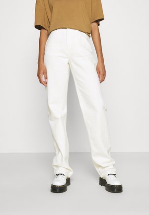 Calças brancas de cintura alta com corte reto, feitas de um tecido texturizado. Usadas com uma blusa oversized castanha e sapatos de plataforma brancos.