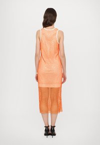 Robe longue en mesh orange avec encolure dégagée, sans manches et fentes latérales. Présente une texture transparente à tissage ouvert.