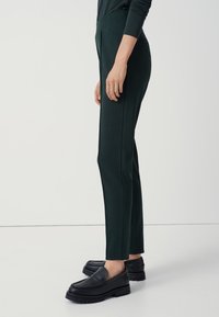 Zielone zwężane spodnie z elastycznej tkaniny, z wysokim stanem i bocznymi kieszeniami, zestawione z masywnymi czarnymi loafersami.