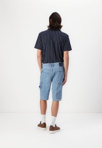 Chemise à rayures bleue marine à manches courtes et shorts cargo bleu clair avec poches, assortis à des chaussures brunes et des chaussettes blanches.
