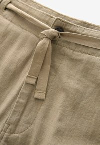 Shorts en lin beige avec une fermeture à cordon, dotés d'un bouton, d'un tissu texturé et de détails de poches latérales.