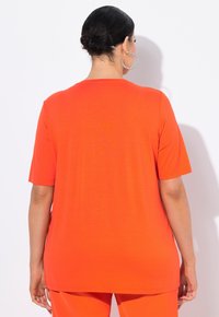 Helles orange T-Shirt mit kurzen Ärmeln, aus weichem Stoff und lässiger Passform. Einfaches Design mit rundem Ausschnitt, ohne Muster oder Akzente.