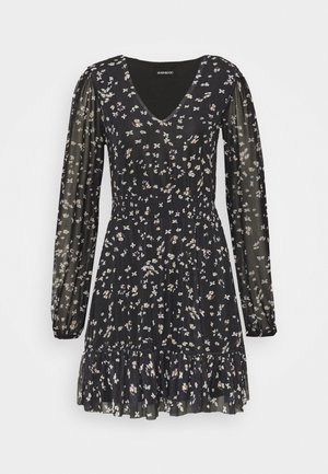 Robe noire à motifs floraux avec de longues manches transparentes, décolleté en V, taille smockée et ourlet à volants en niveaux. Présente des petits motifs floraux colorés.
