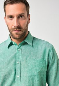 Camisa verde de mezcla de lino con botones, textura sutil, bolsillo en el pecho izquierdo y diseño clásico de cuello.